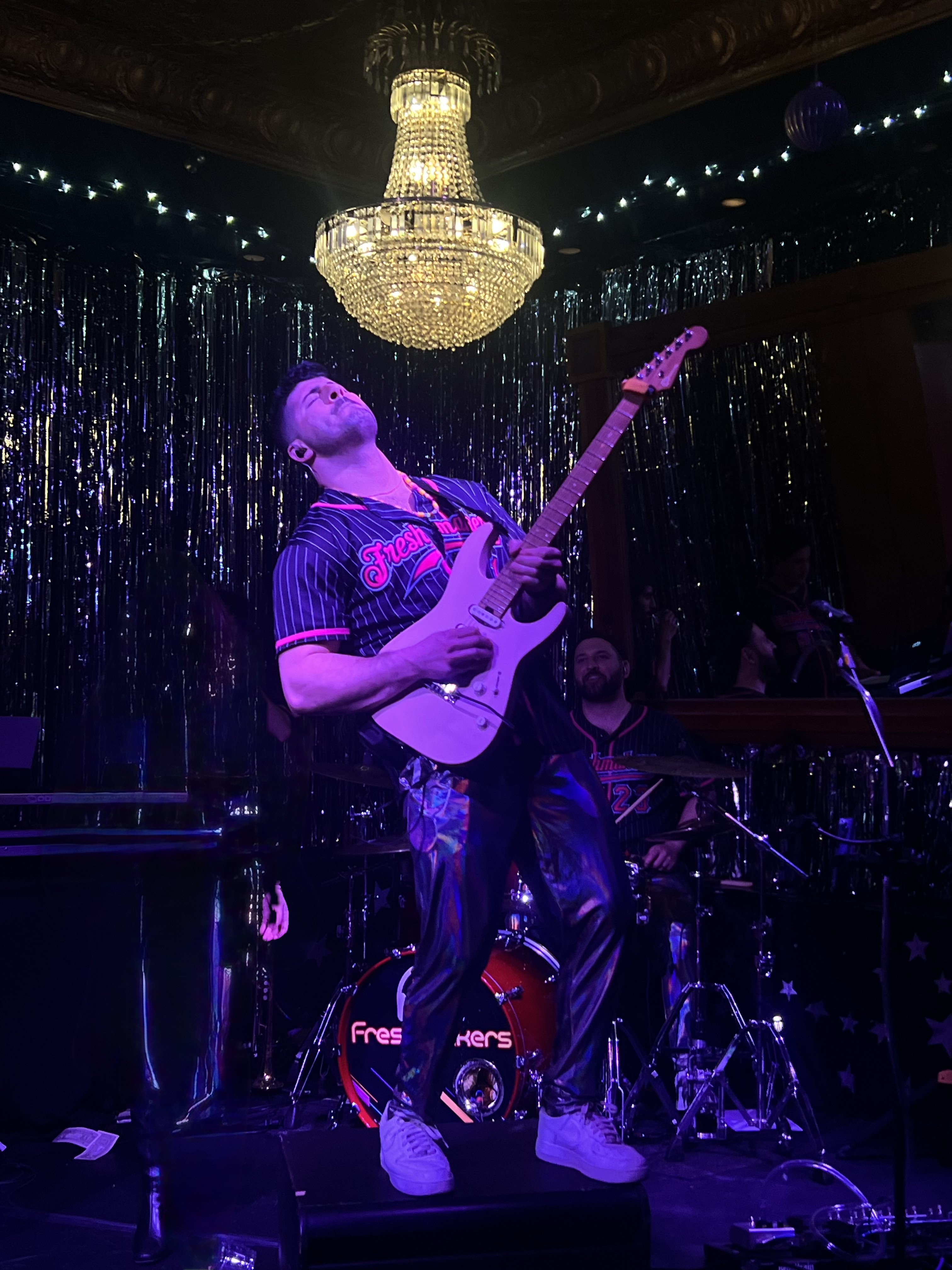 Spotlight guitarist mid-solo under a chandelier at a club show